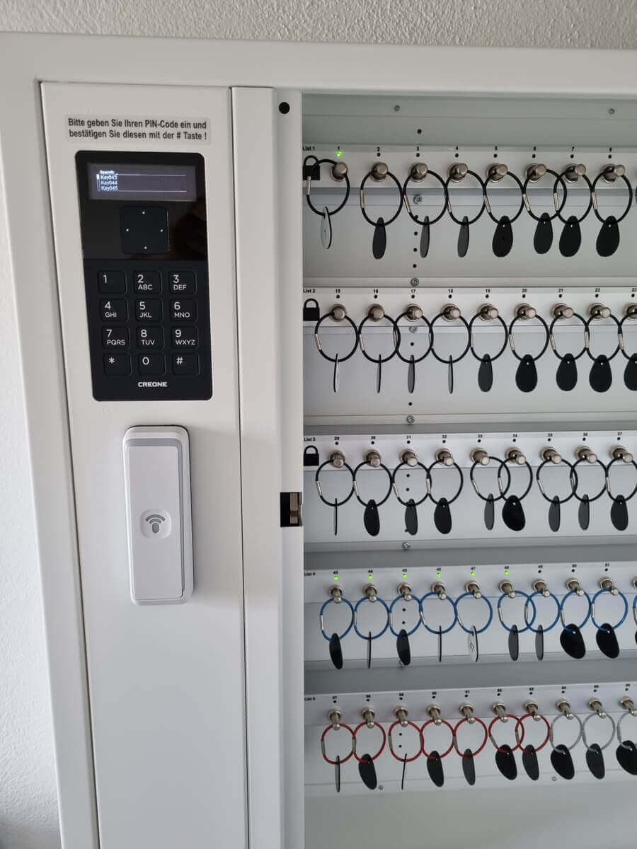 Detailansicht eines elektronischen Schlüsselschranks mit PIN-Code-Eingabe, modernen schwarzen und farbigen Schlüsselringen und digitalem Bedienfeld