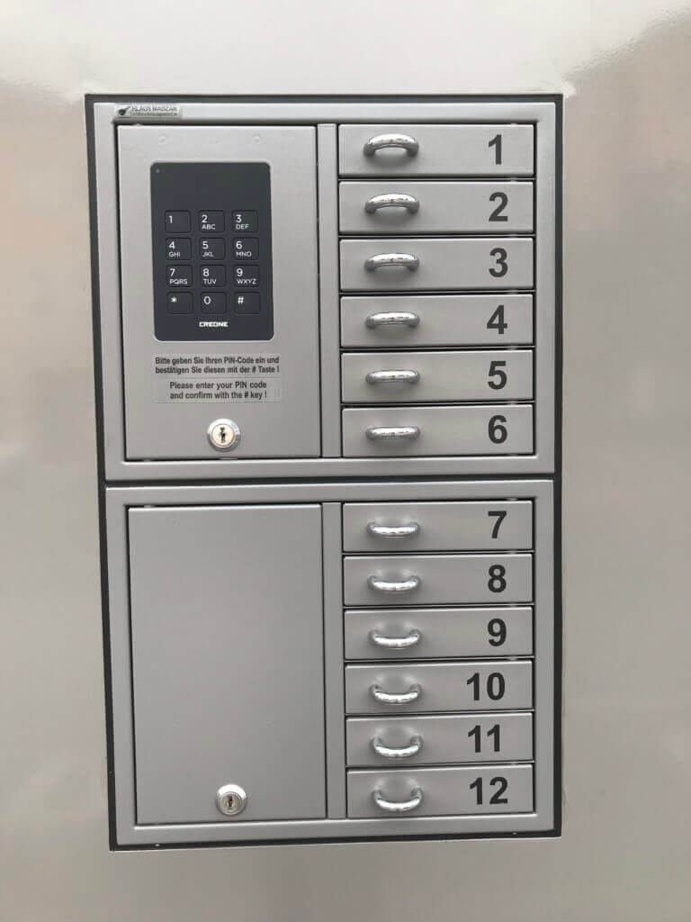 Silberne Schließfachanlage mit zwölf nummerierten Fächern und PIN-Code-Tastatur zur sicheren Aufbewahrung