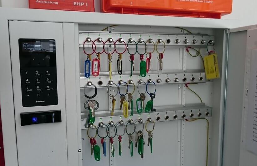 Offener Schlüsselschrank mit elektronischem Zahlenschloss und verschiedenen Schlüsseln an farbigen Anhängern