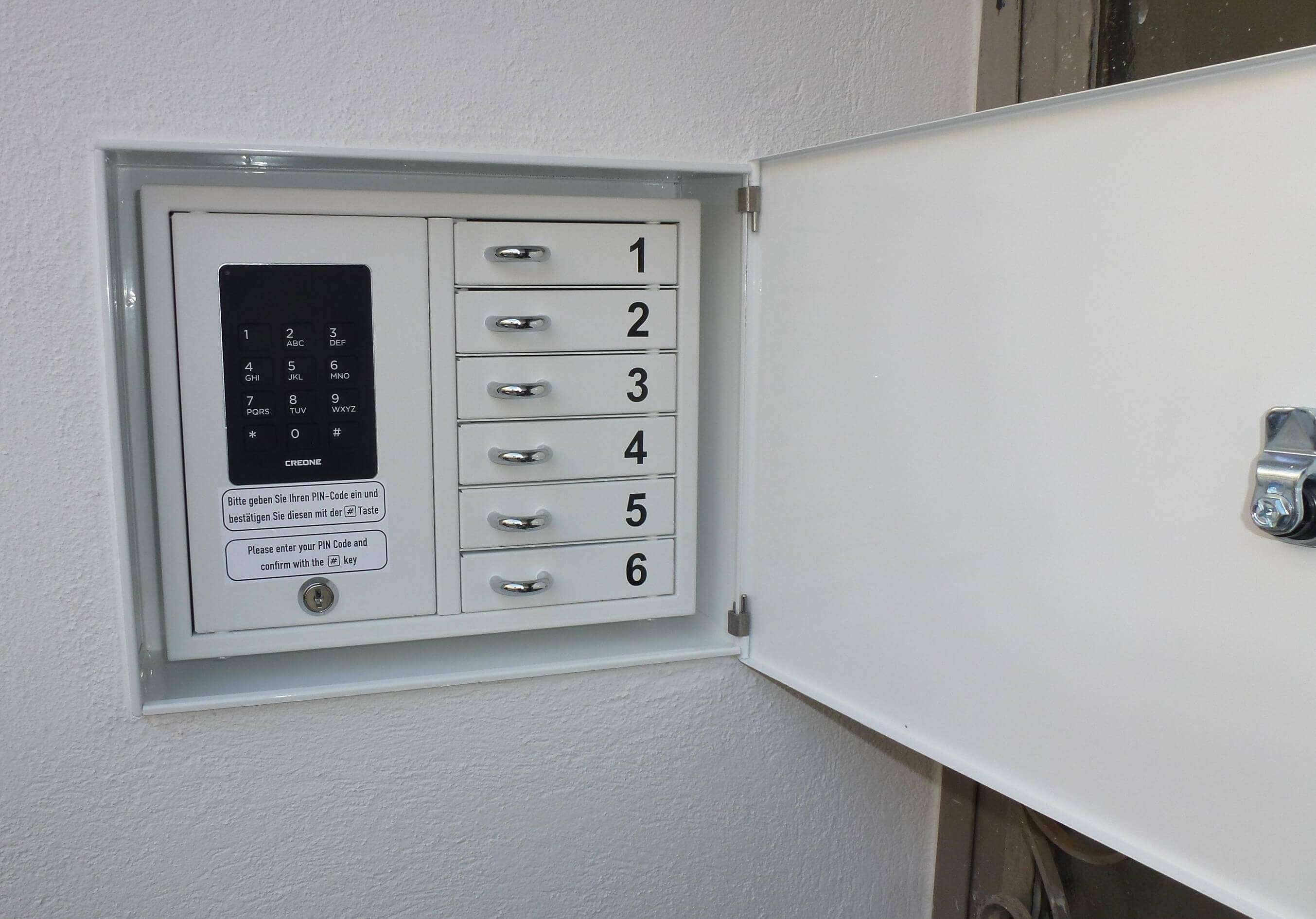 Metallisches Schlüsseldepot mit sechs nummerierten Fächern und elektronischer PIN-Tastatur zur sicheren Schlüsselverwahrung an der Wand