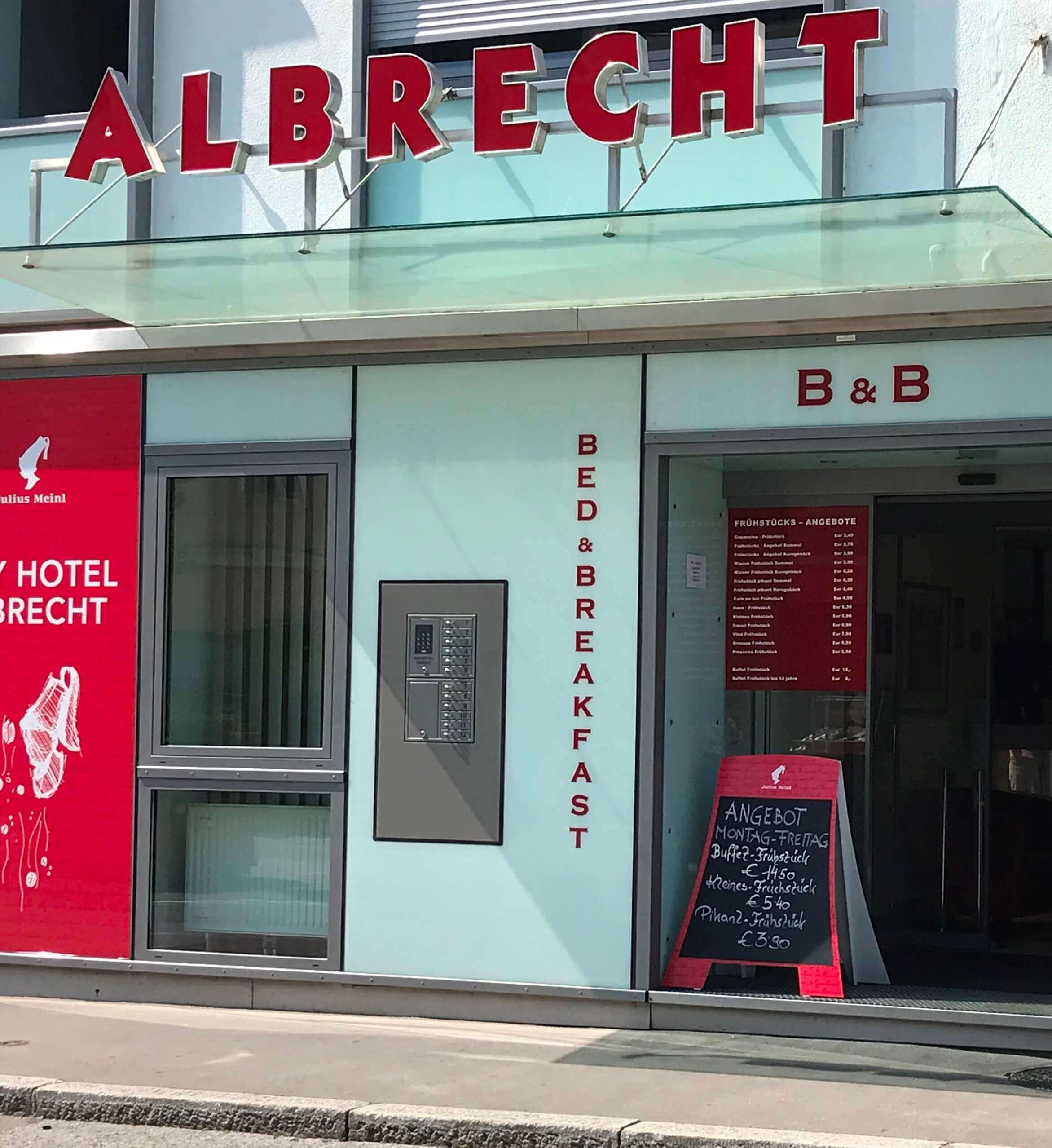 Vorderansicht des Hotels Albrecht mit dem Schriftzug 'Bed & Breakfast', einem roten Werbeplakat und einer Tafel mit Frühstücksangeboten vor dem Eingang.