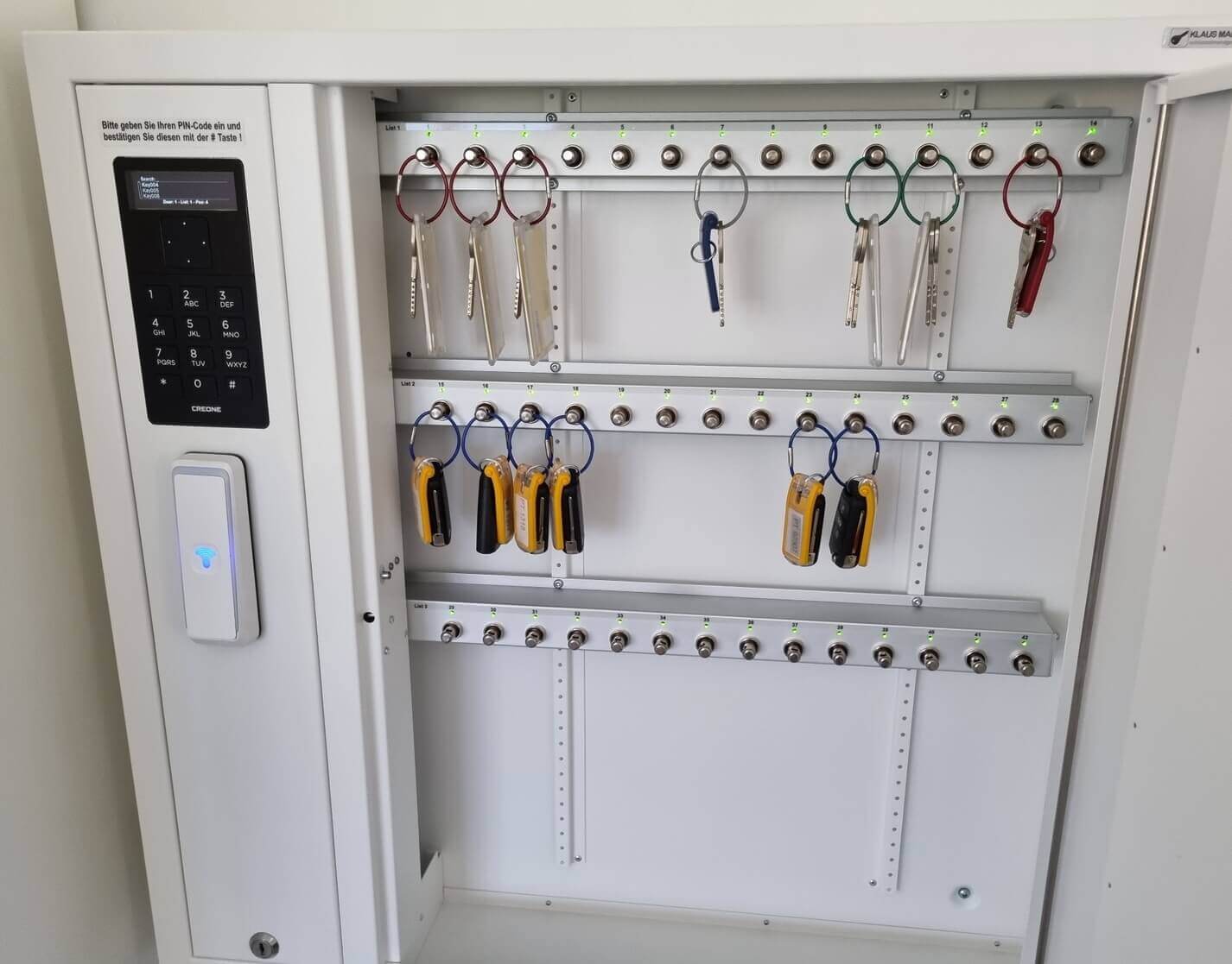 Offener elektronischer Schlüsselschrank mit zahlreichen Schlüsseln und Transpondern an nummerierten Haken, Bedienfeld mit PIN-Eingabe sichtbar
