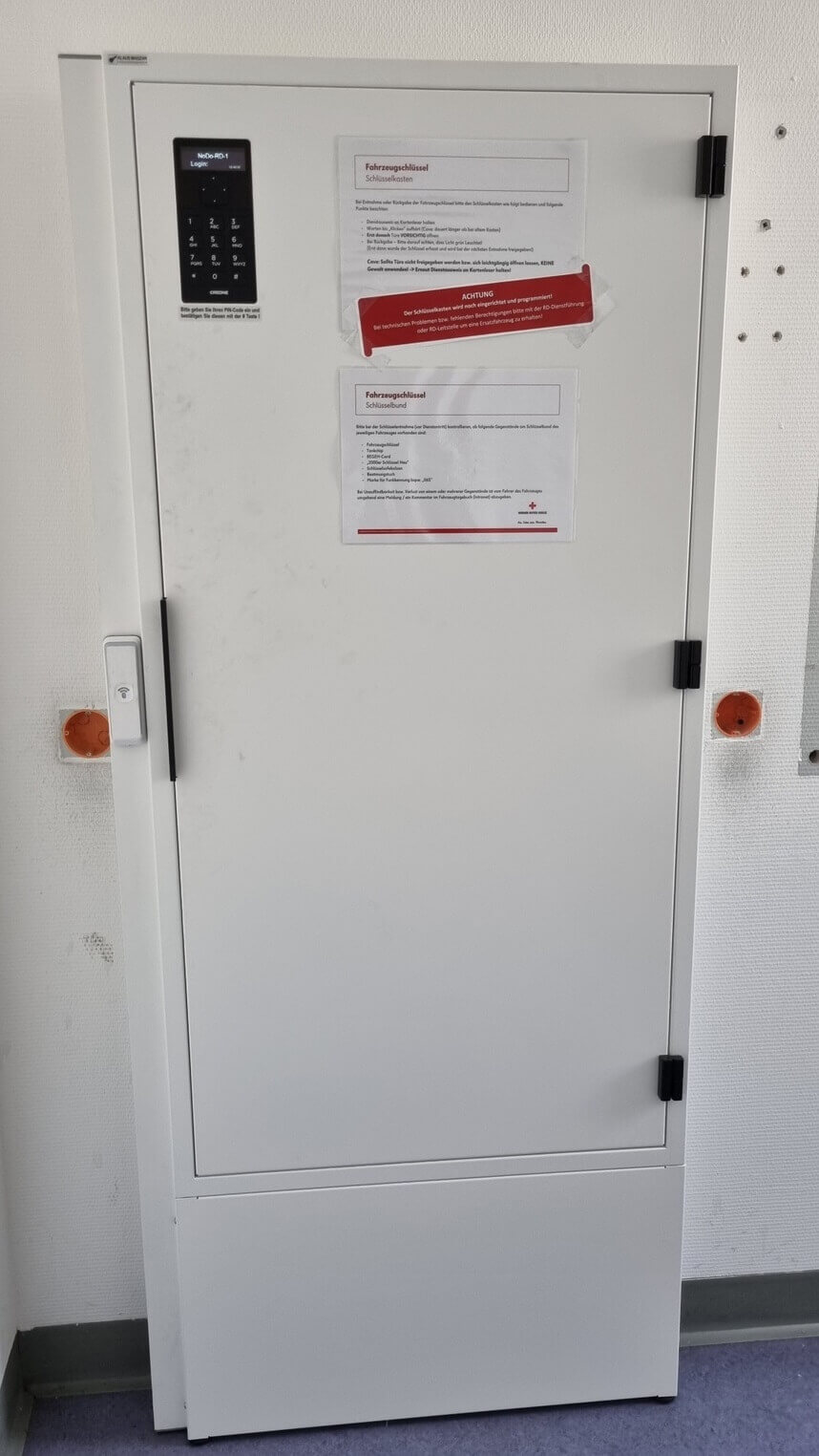 Weißer Schlüsselschrank mit elektronischem Zahlencode und zwei Informationsblättern an der Tür, geeignet zur sicheren Aufbewahrung von Fahrzeugschlüsseln