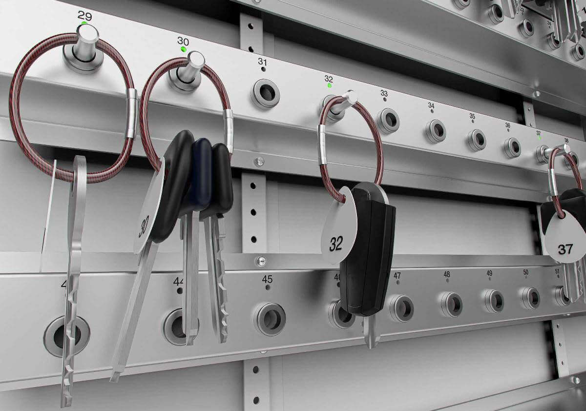 Mehrere Schlüssel und Autoschlüssel hängen an nummerierten Haken in einem modernen Schlüsseldepot.