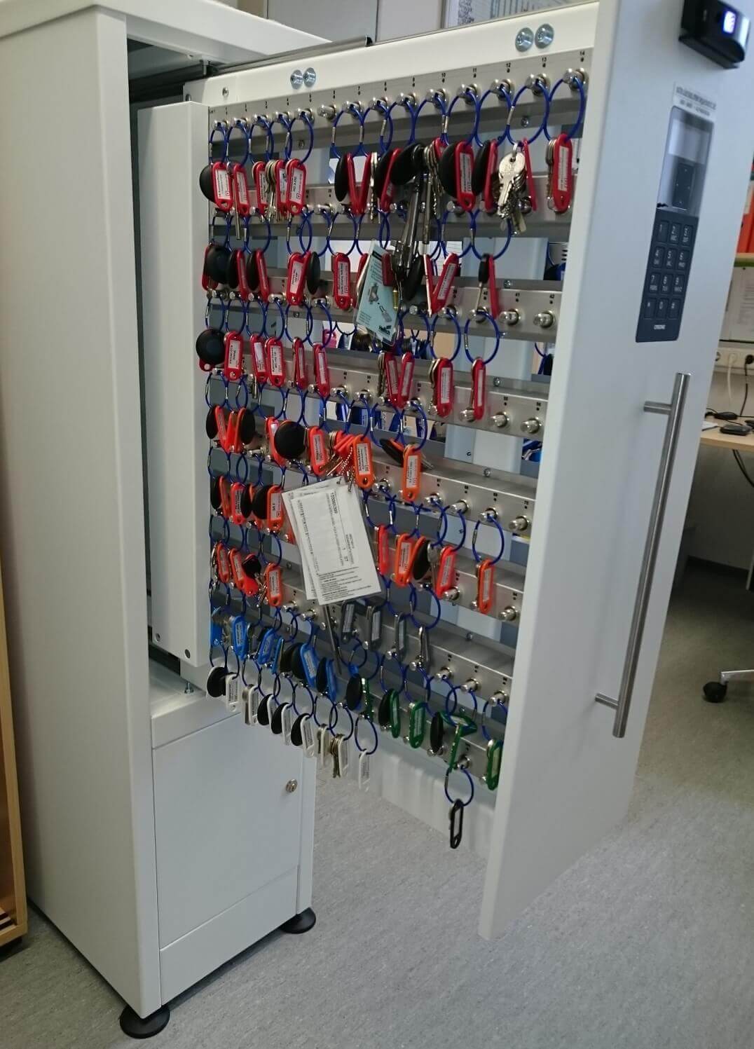 Offener elektronischer Schlüsselschrank mit vielen Schlüsseln und beschrifteten Anhängern, geeignet für Büros oder Unternehmen