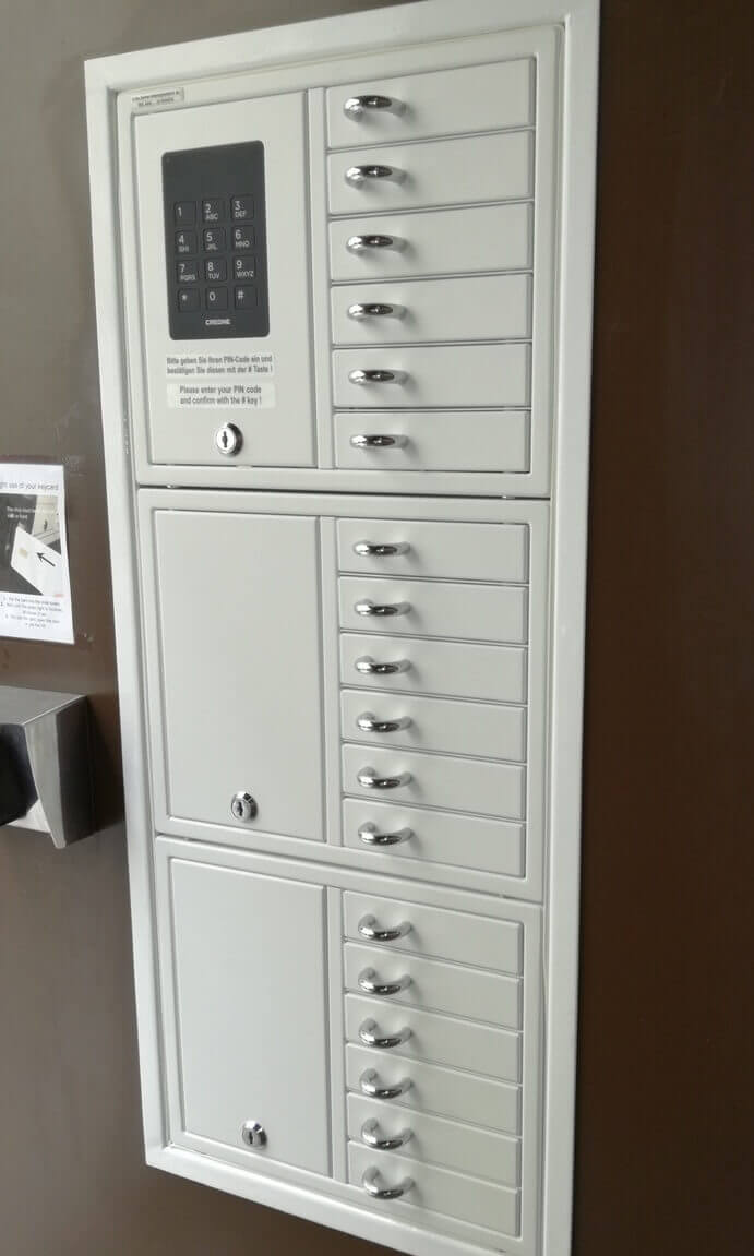 Elektronischer Schlüsselschrank aus Metall mit PIN-Tastatur und zahlreichen einzelnen Fächern, montiert an einer Wand