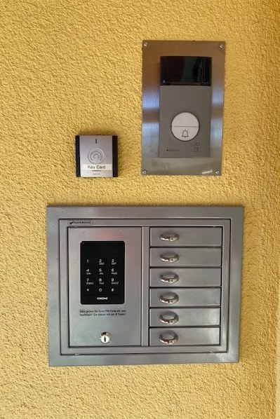 Elektronische Türsprechanlage mit Kamera, Key Card-Leser und mehreren Briefkästen auf gelbem Putz