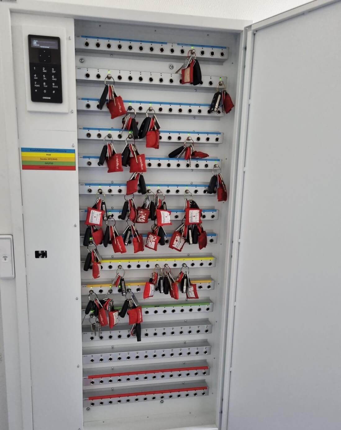 Geöffneter elektronischer Schlüsselschrank mit vielen Schlüsseln an Haken und Zahlencode-Tastatur