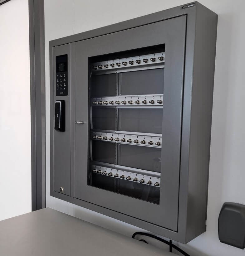 Abgebildet ist ein moderner, an der Wand montierter Schlüsselschrank mit elektronischem Zugangssystem und mehreren beschrifteten Haken zur organisierten Schlüsselaufbewahrung.